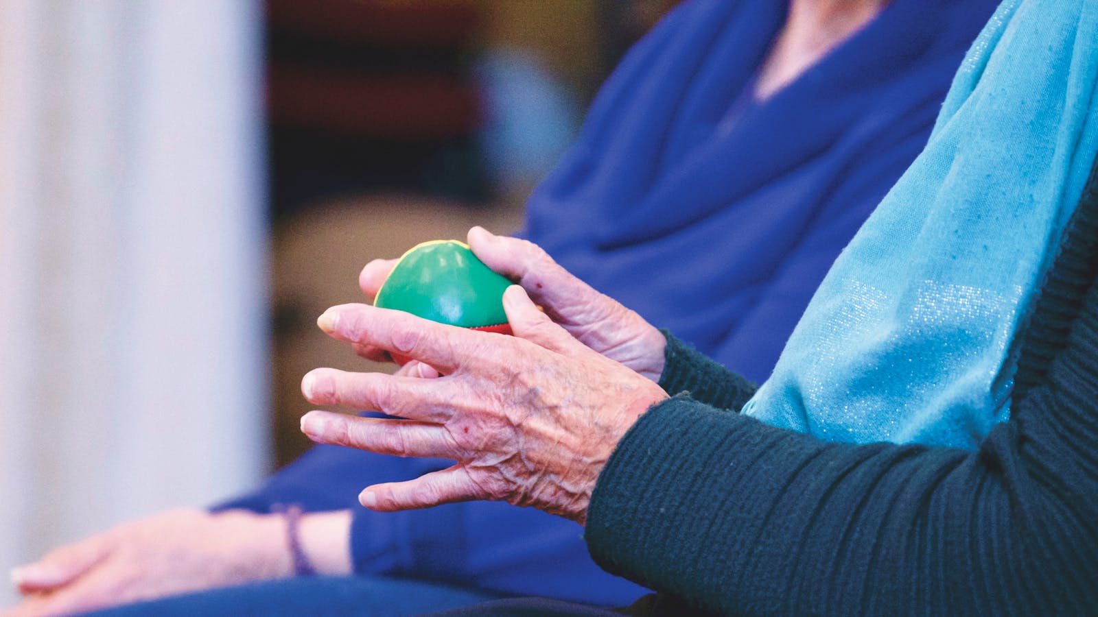 Close-up of senior person's hands holding a green therapy ball, showcasing wrinkles and care.